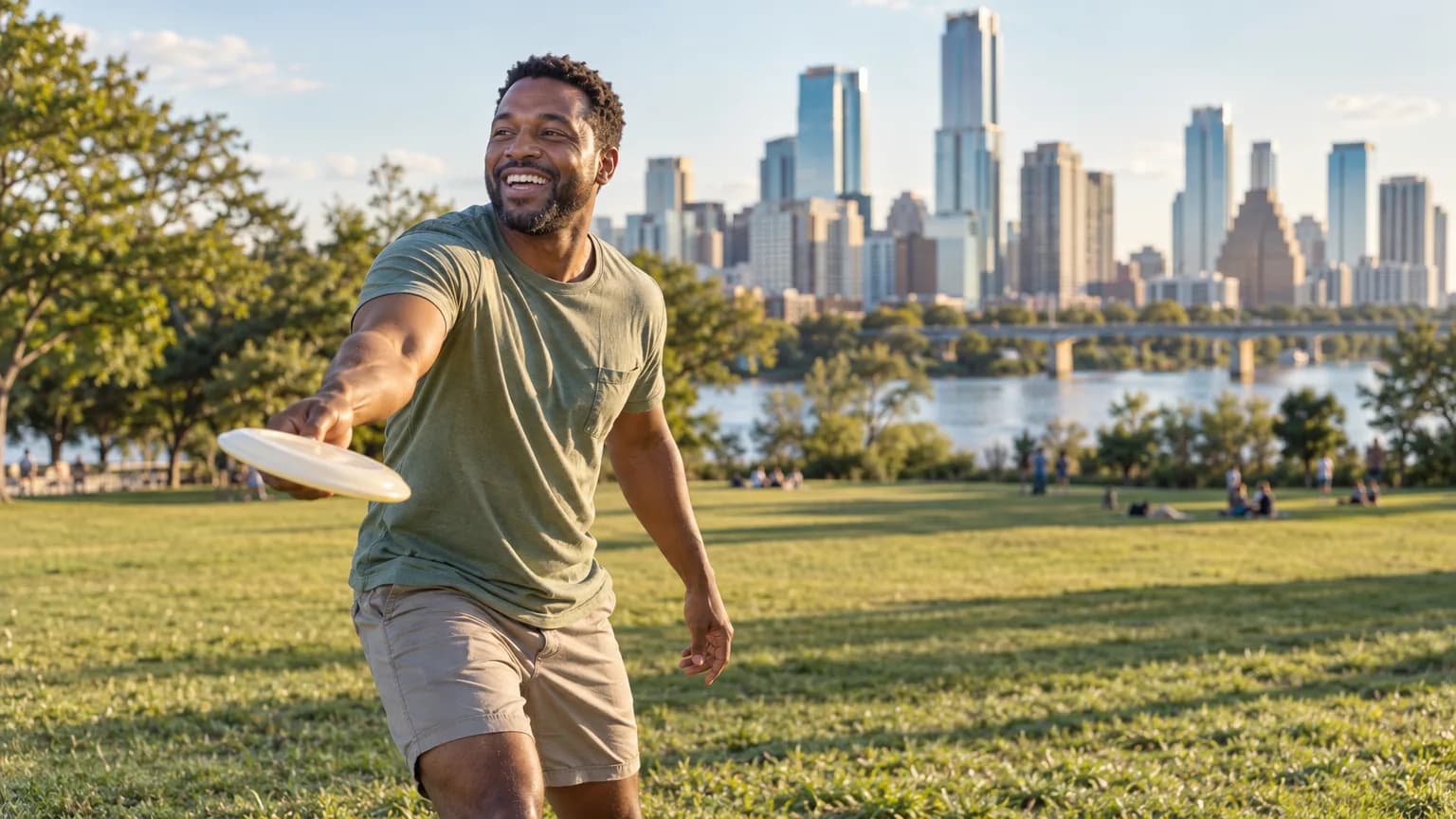 A man tossing a frisbee on the lawn at Zilker Park with the Austin skyline behind him