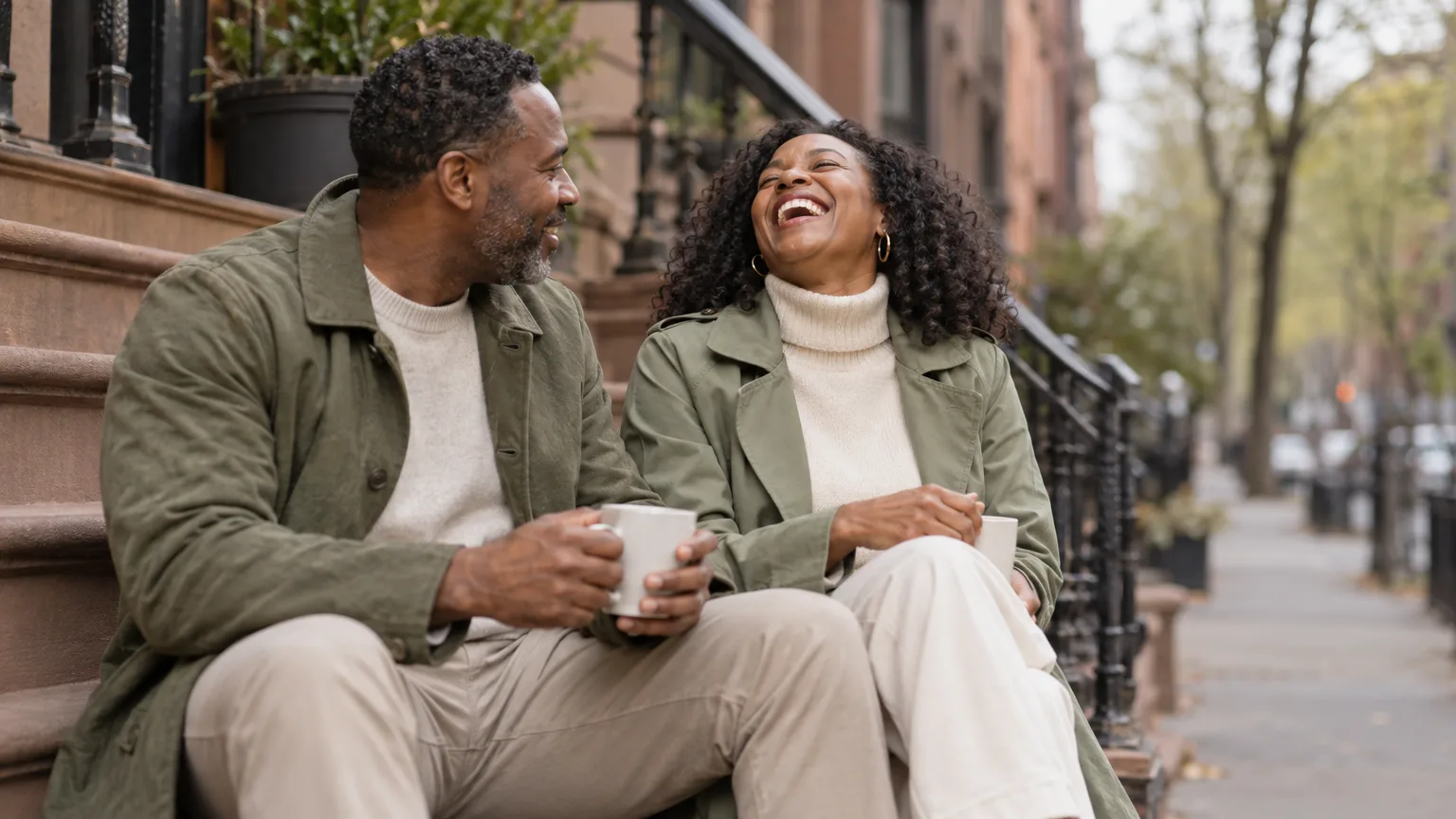 A couple laughing over coffee on a brownstone stoop in New York.